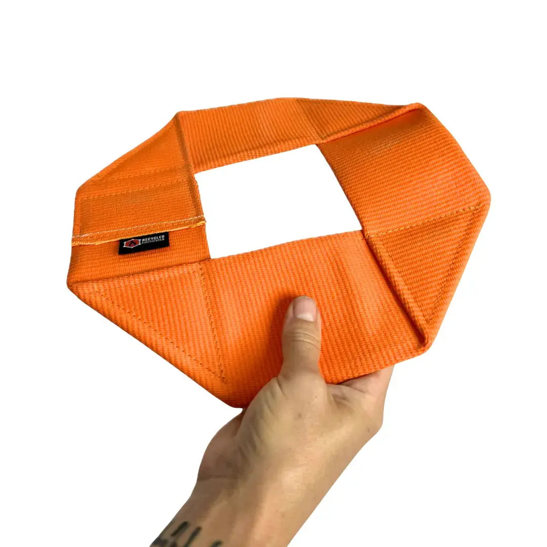 Orange fire hose frisbee dog toy held in a hand.