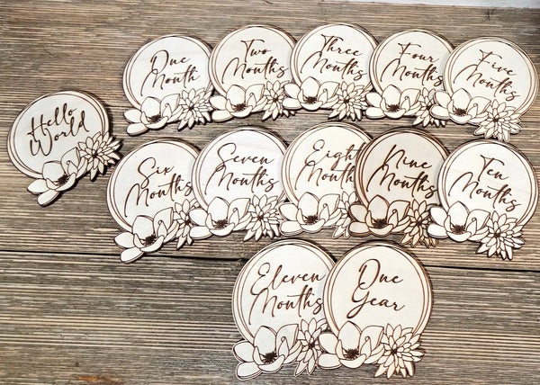 Wooden baby milestone discs featuring floral designs for monthly growth tracking, set on a wood background.