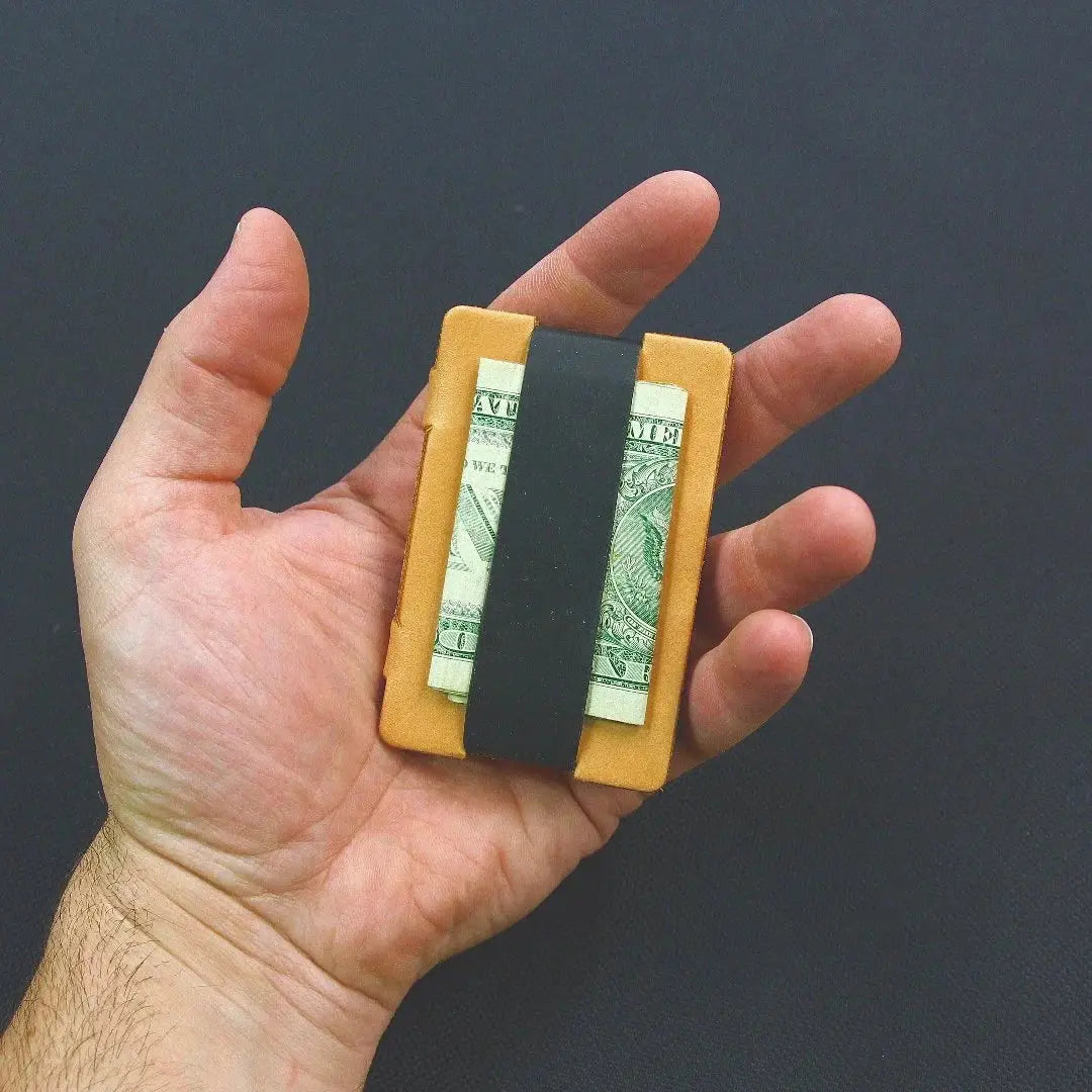 Leather card wallet with folded bills held by an elastic strap in a hand