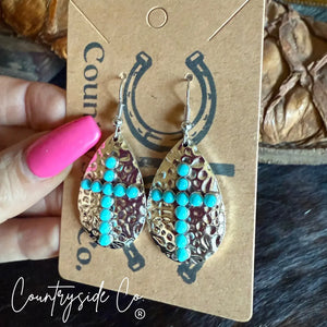 Hammered silver cross dangle earrings with turquoise beads on a card.