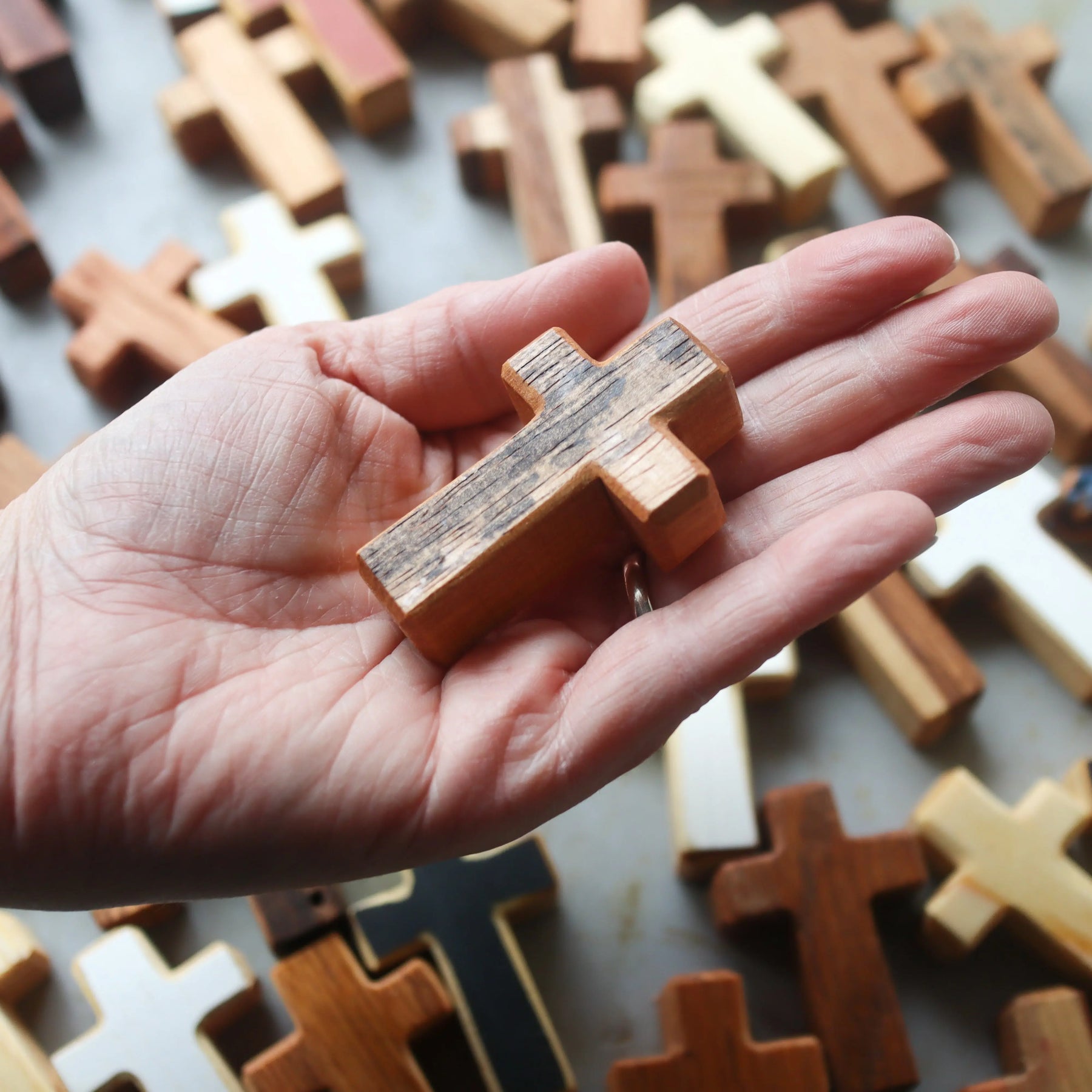 Handmade wooden pocket cross held in a person's palm, surrounded by other crosses.