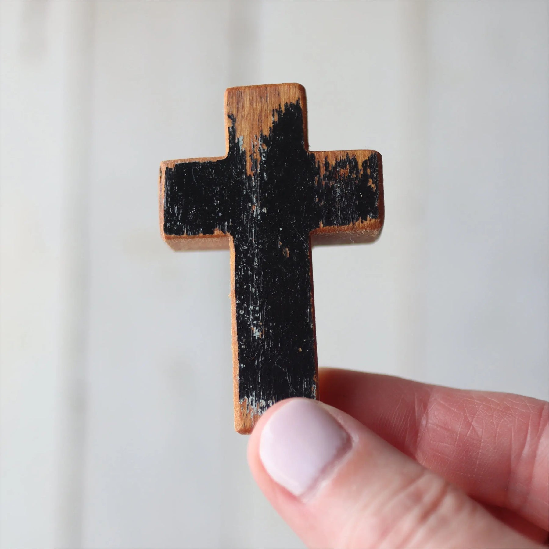 A hand holds a small, worn wooden cross with black paint.