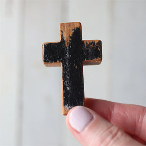 A hand holds a small, worn wooden cross with black paint.
