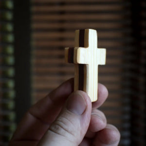 Hand holding a small wooden cross with darker stripes.