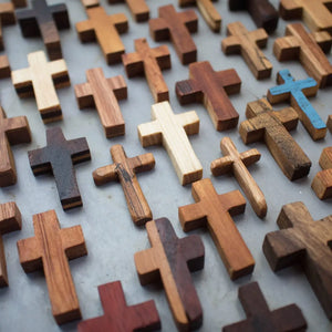 Assortment of pocket-sized wooden crosses in various wood tones and styles.