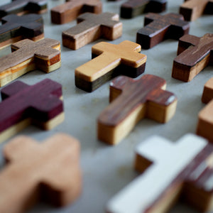 Assortment of wooden pocket crosses in various wood tones arranged on a gray surface.