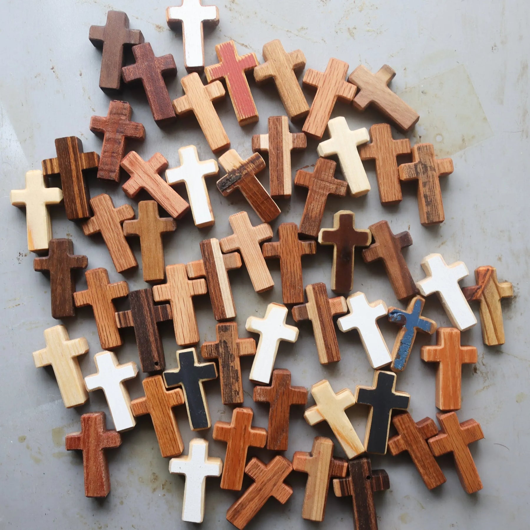 Assorted handmade wooden crosses scattered on a textured gray surface.