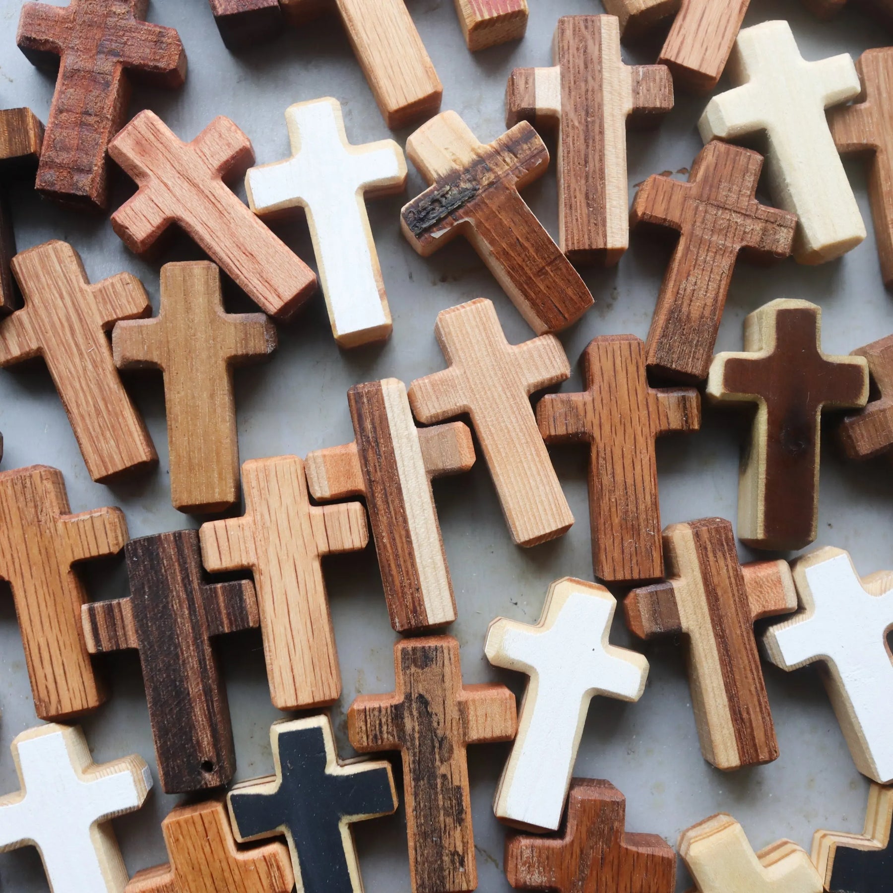 Assortment of handmade wooden crosses in various wood tones and some painted white and black.