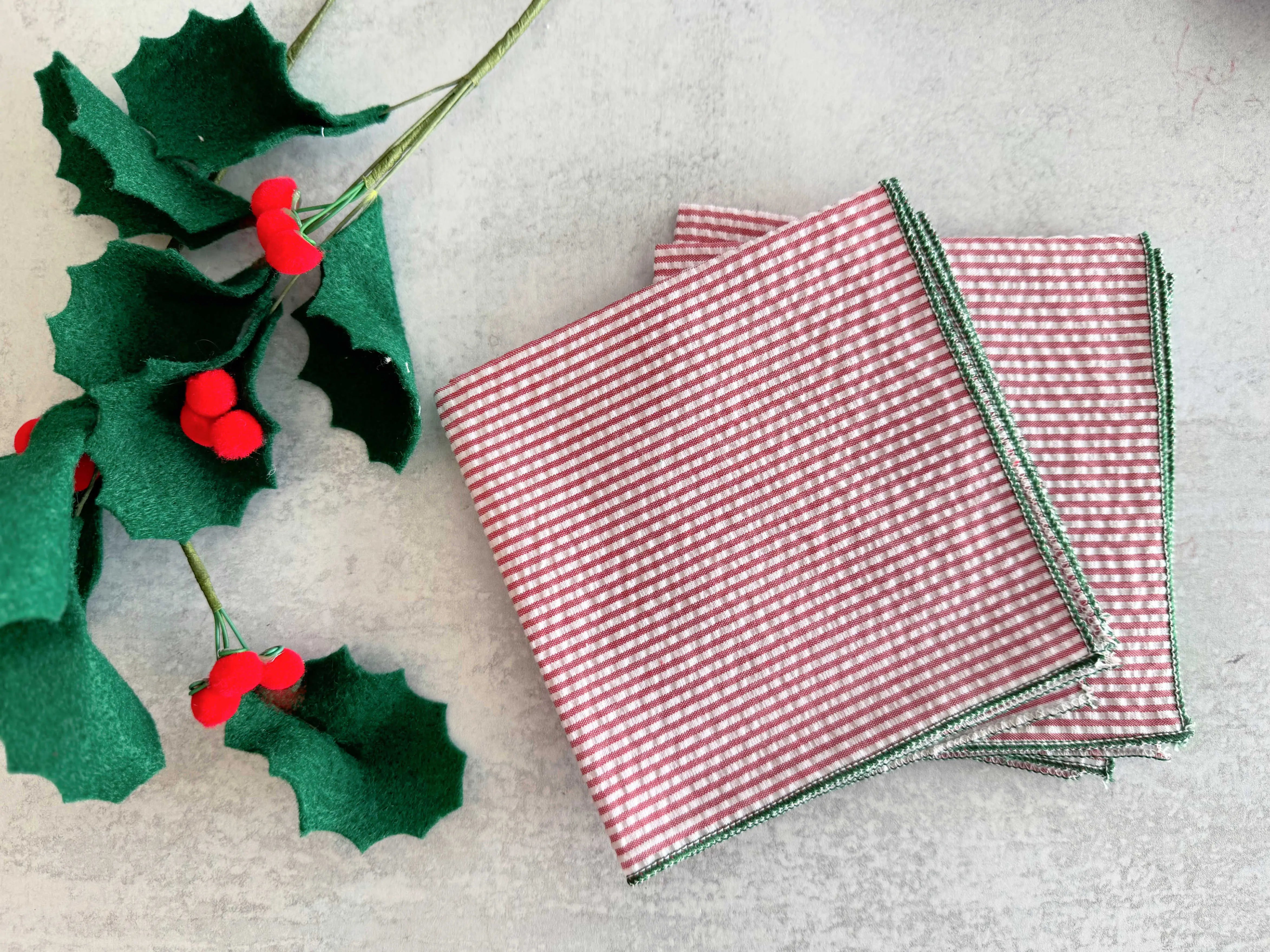 Christmas holly leaves with red berries and red and white striped napkins with green trim.