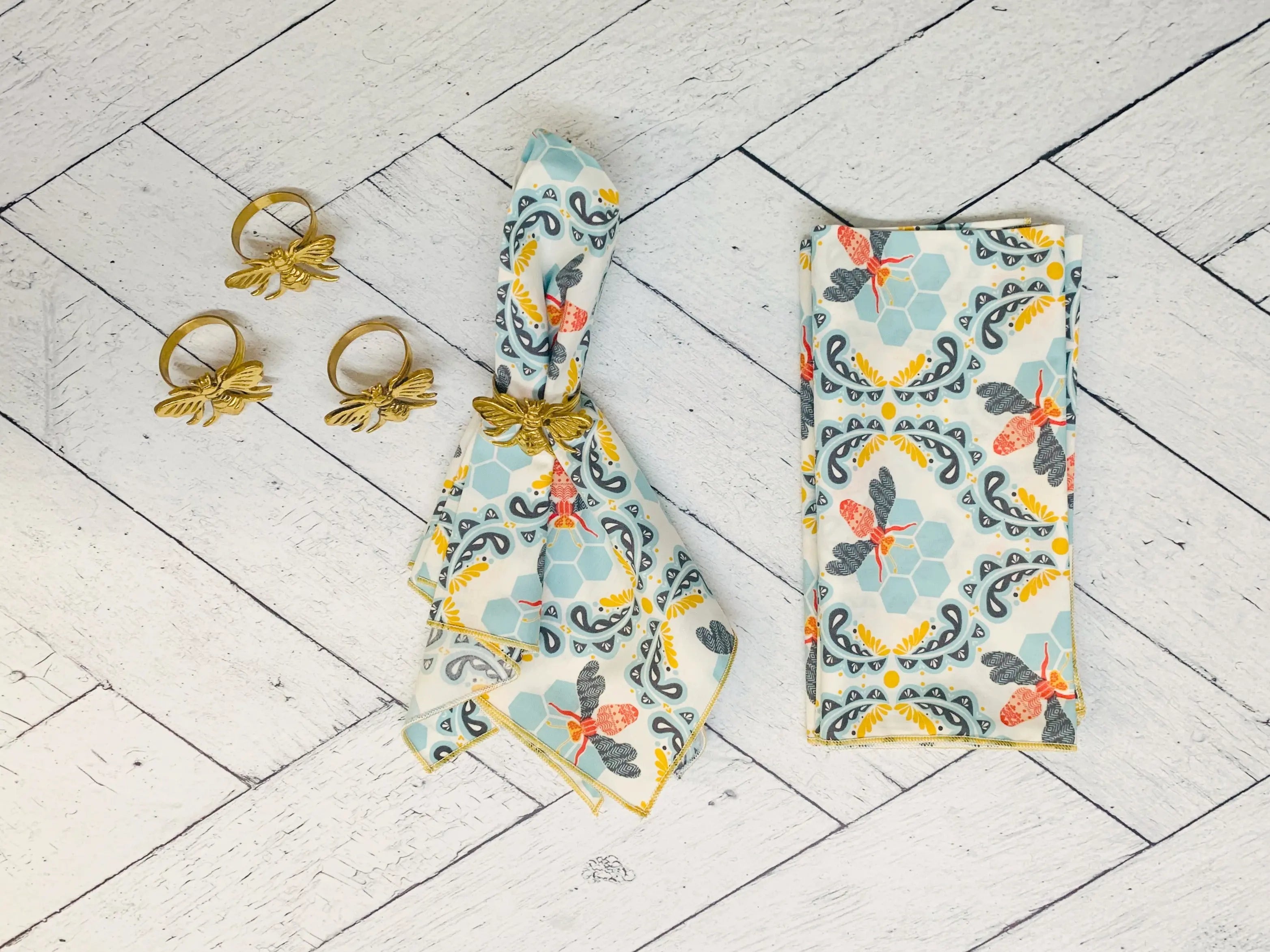 Cotton honey bee cloth napkins and gold bee napkin rings on white wood background.