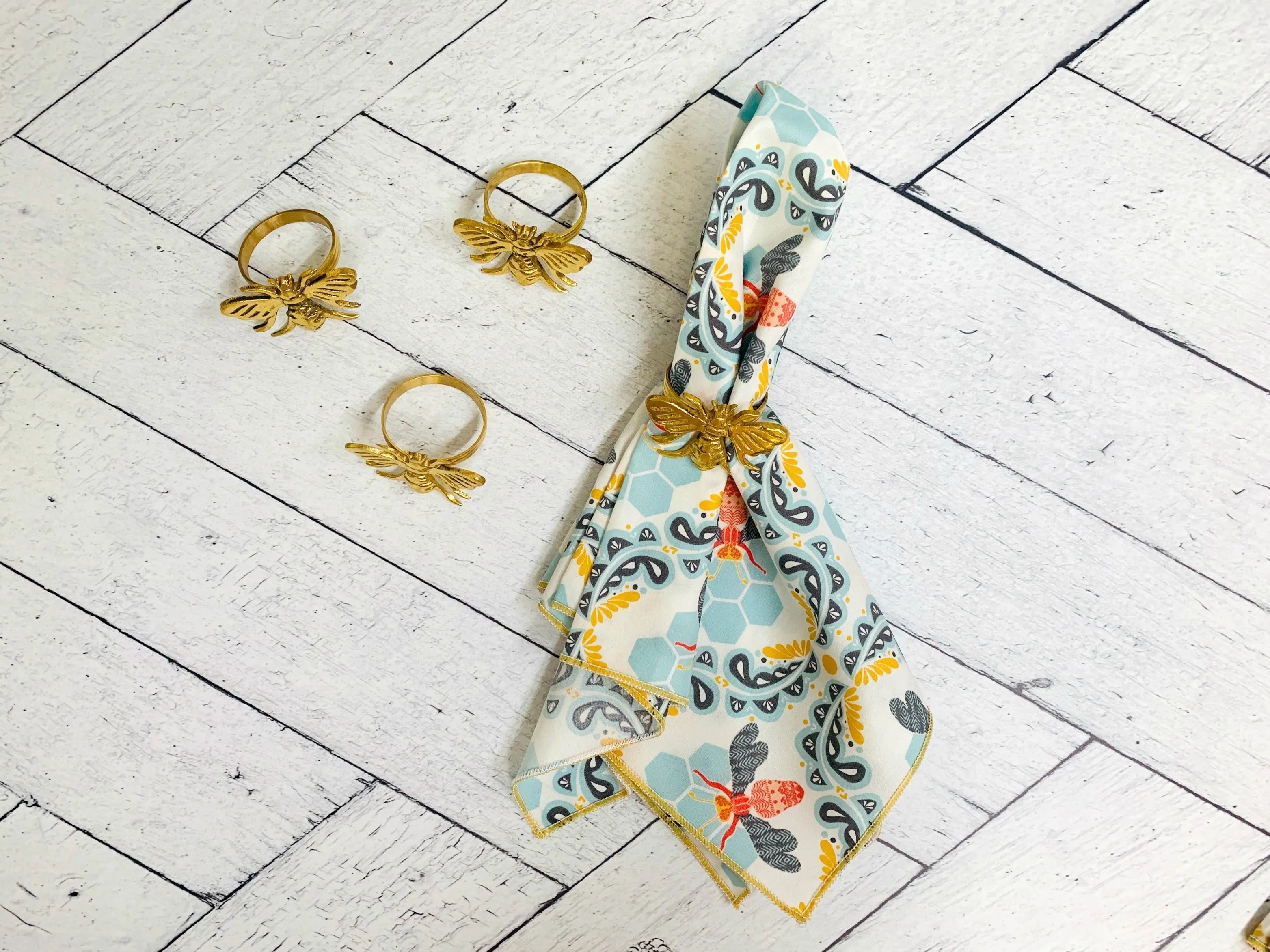 Set of four honey bee cloth napkins and gold bee napkin rings on a white wooden background.