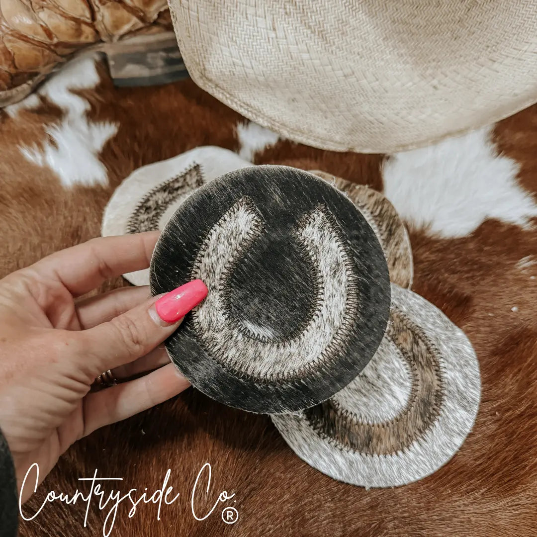 Horseshoe cowhide coasters with stitched edges on a brown and white cowhide background.