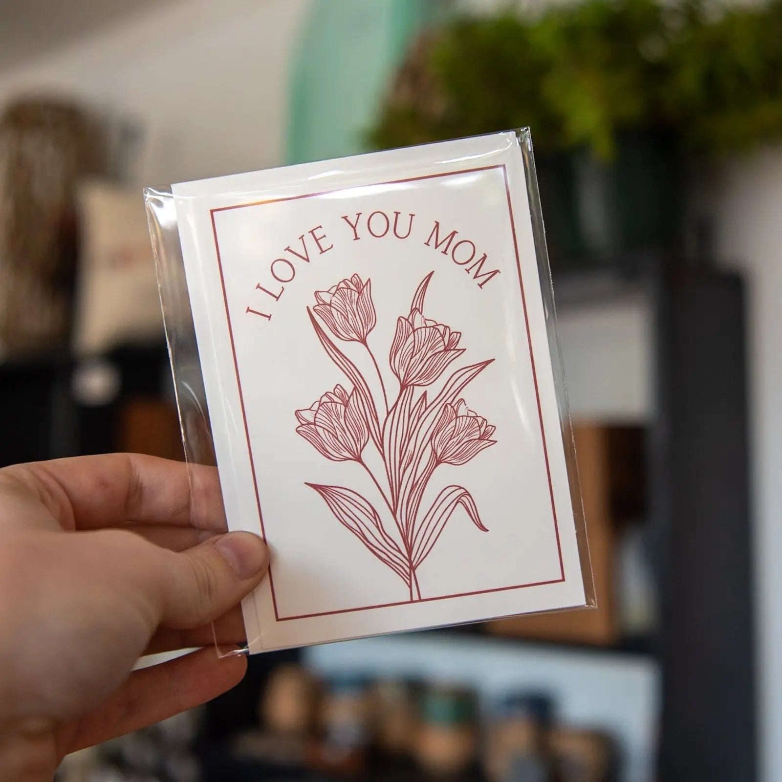 A white greeting card with red tulip illustrations and the text "I LOVE YOU MOM".