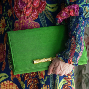 Emerald green silk clutch with gold bamboo clasp held by a hand.