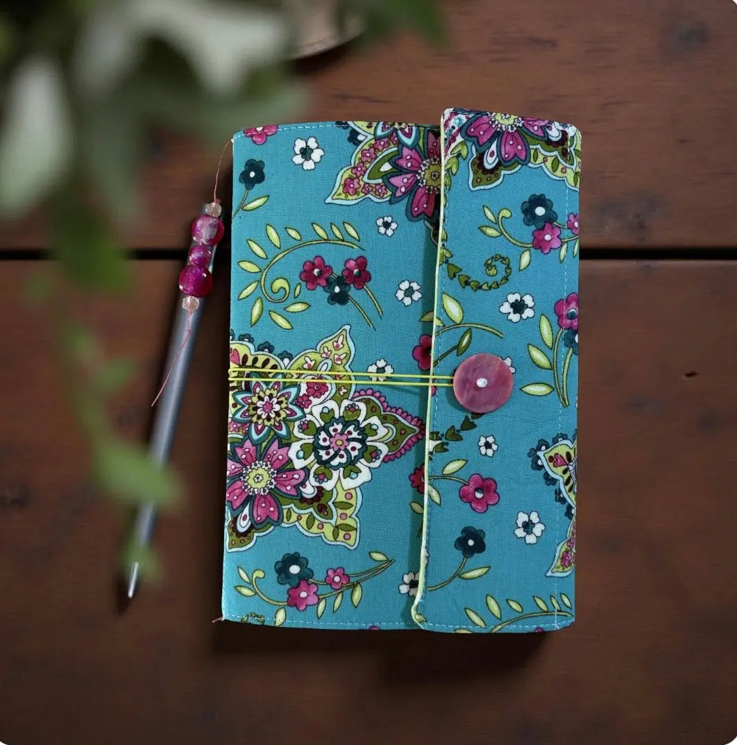 Floral fabric journal with pen and button closure on a wood surface. Handmade notebook with a snap closure.