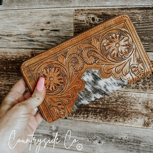 Tan tooled leather cowhide wallet with floral patterns and a zipper closure.