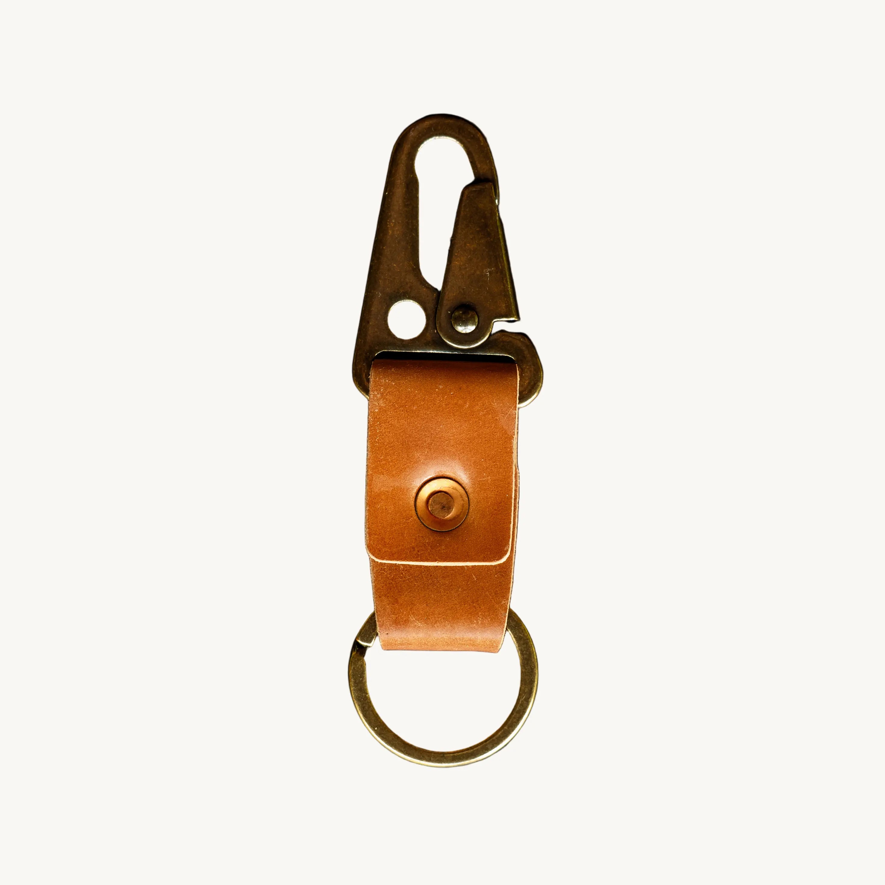 A key clip with brown leather strap, a brass lever clip, and an antique brass key ring on a white background.