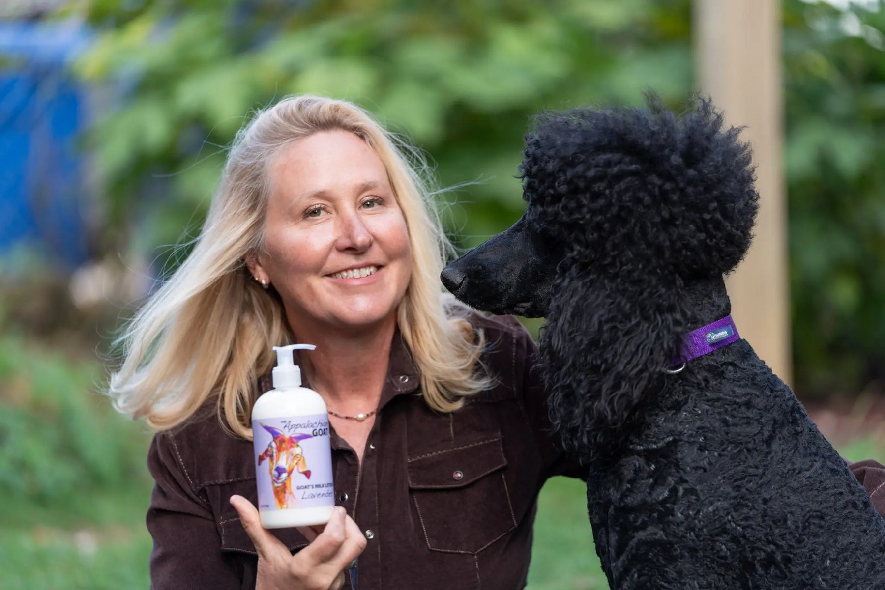 Woman holding lavender goat's milk lotion next to black poodle