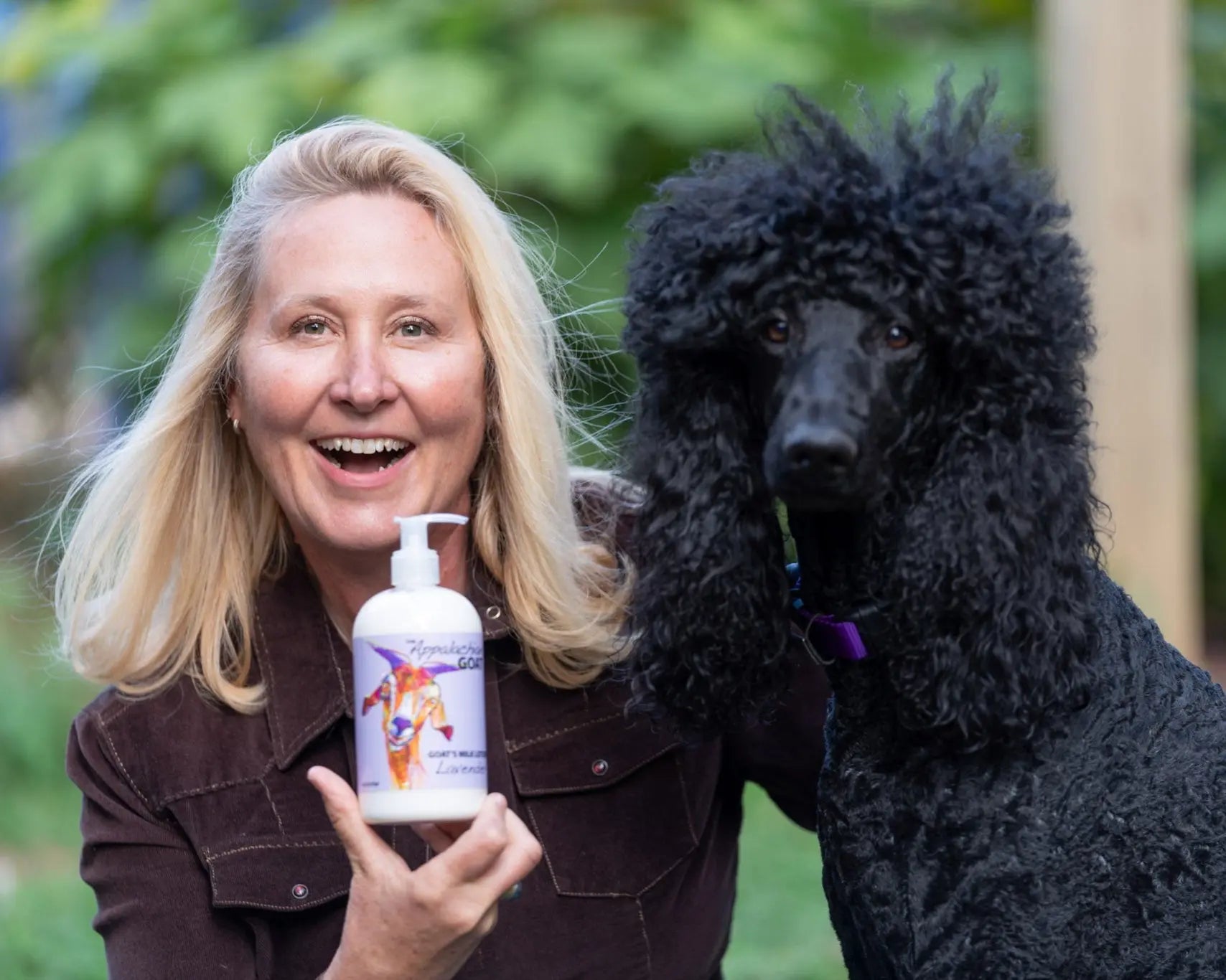 Lavender goat milk lotion bottle held by a woman next to a black poodle.