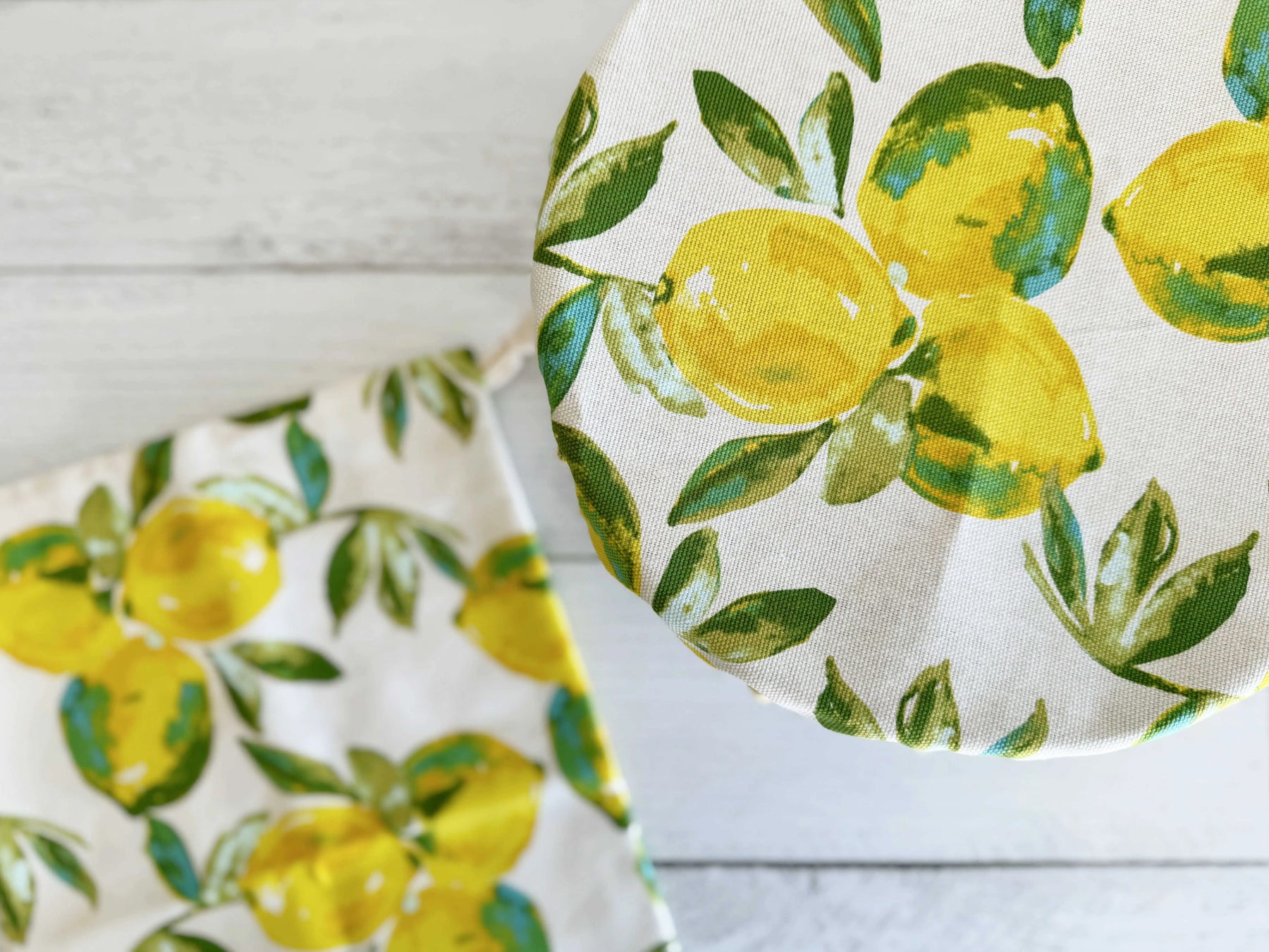 Linen bread bag and cover with yellow lemons and green leaves pattern on white wooden background.