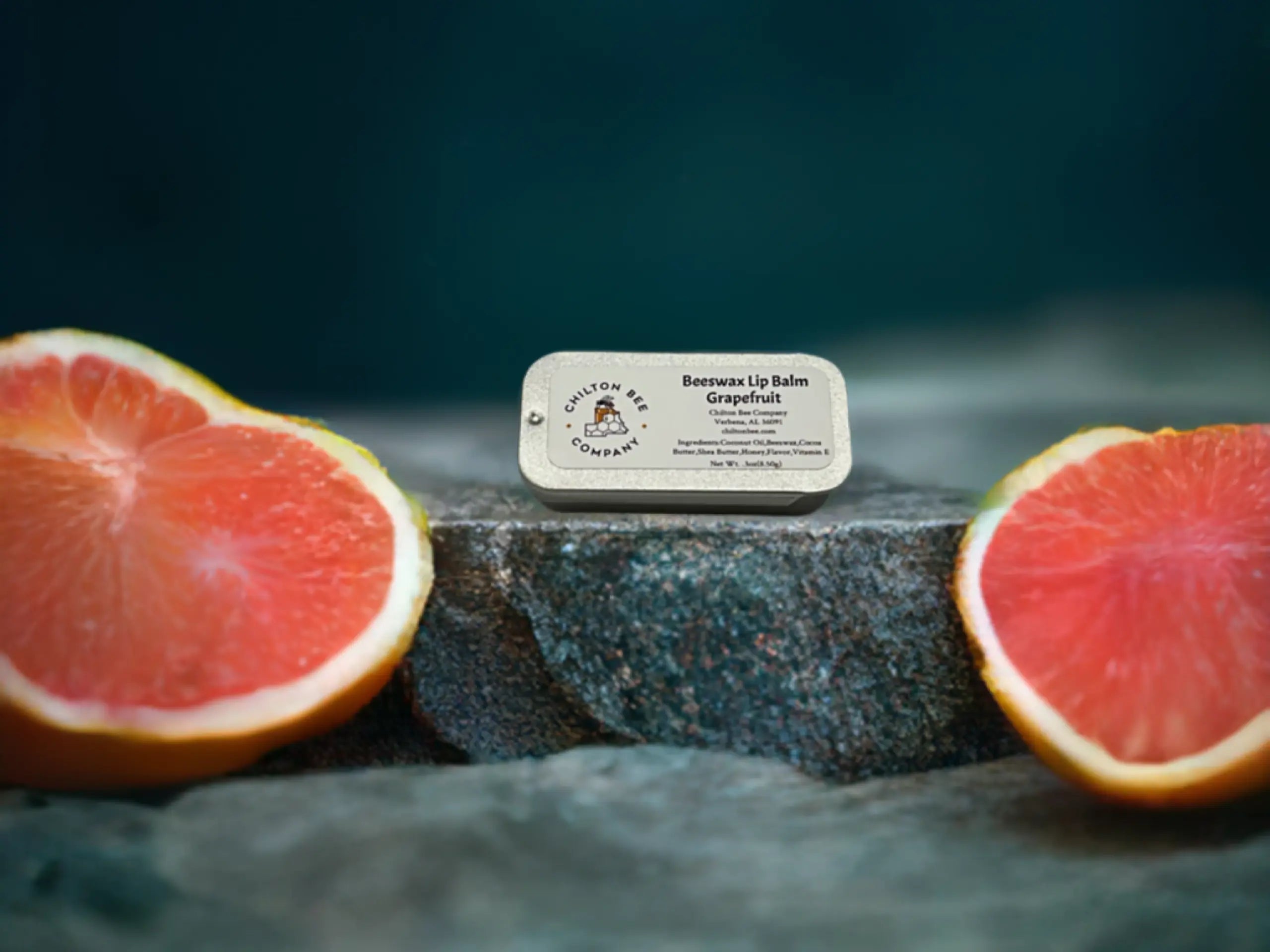 Chilton Bee grapefruit lip balm tin between grapefruit halves on a rock surface. 