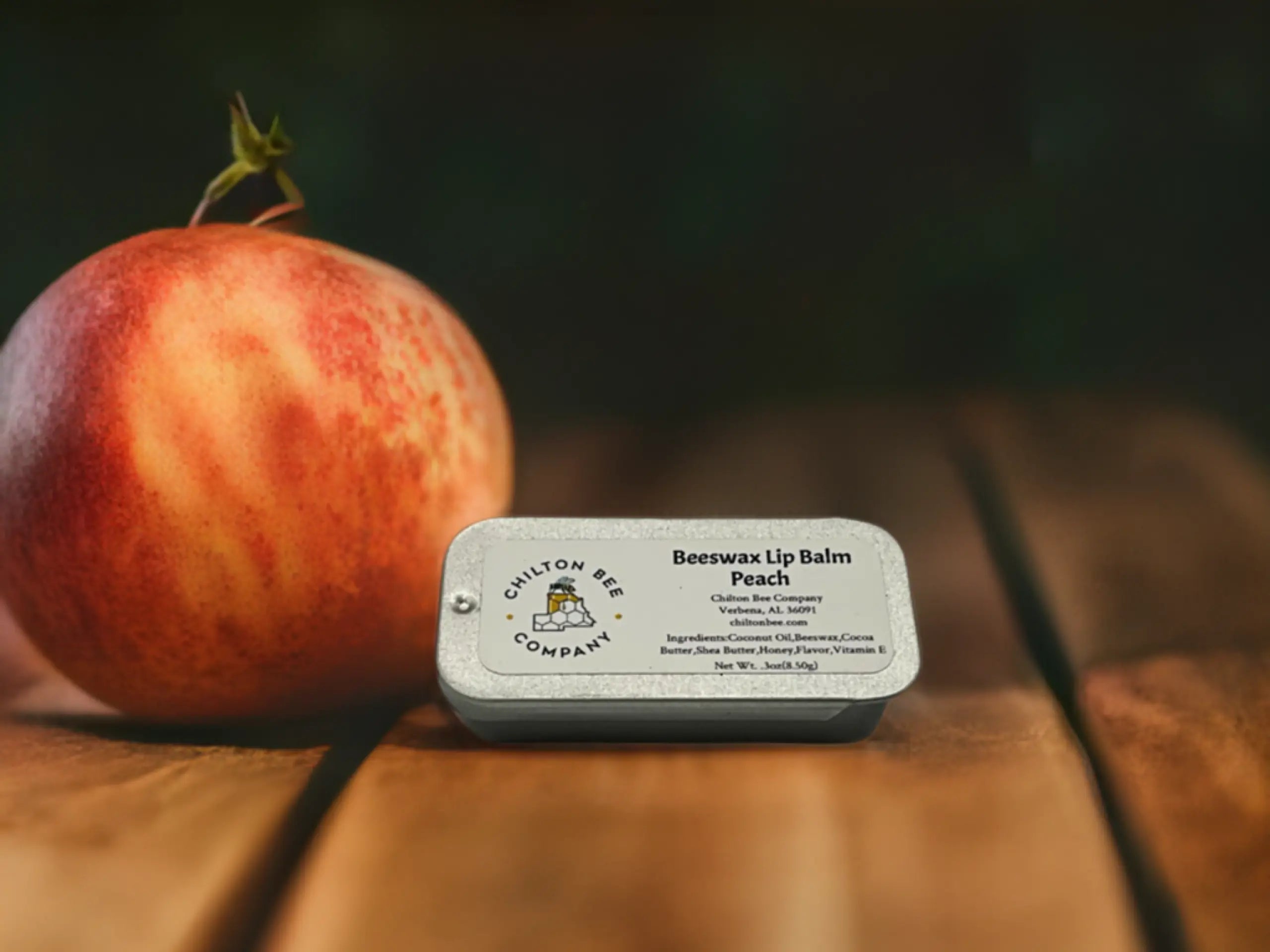 Peach lip balm tin by Chilton Bee Company with a real peach on a wooden surface
