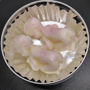 Lotion bars shaped like babies with pink accents in a metal tin with cupcake liner.