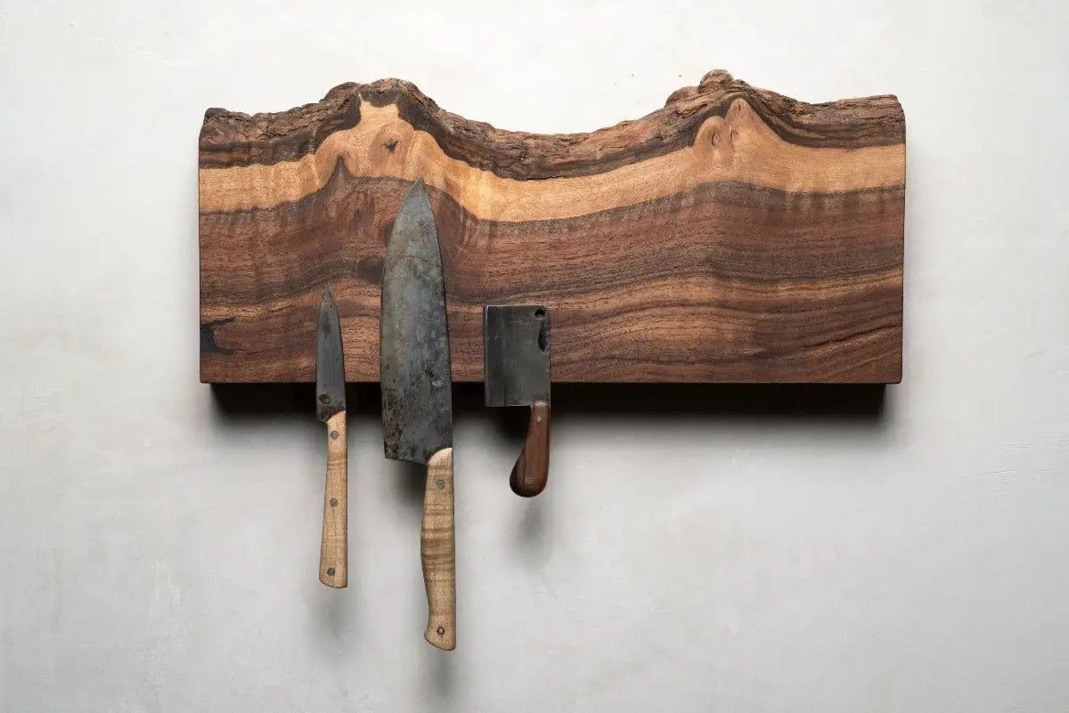 Wooden magnetic knife holder with live edge holding three knives against a light wall.
