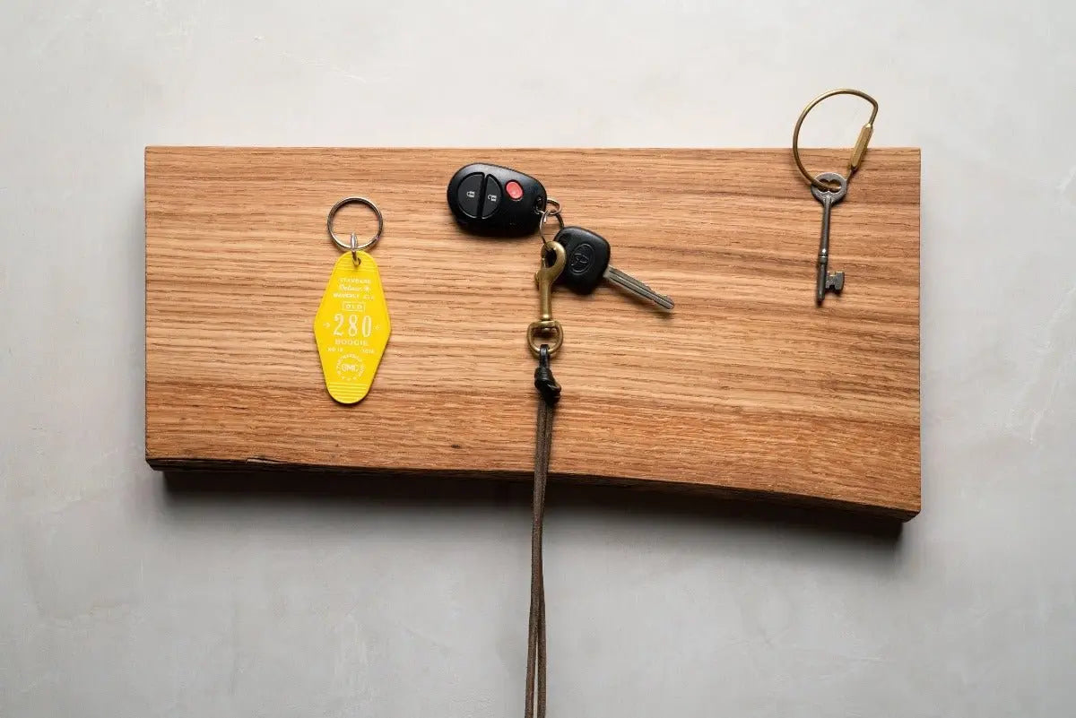 Wooden key holder made of oak with keys and a key fob attached, mounted on a gray wall.