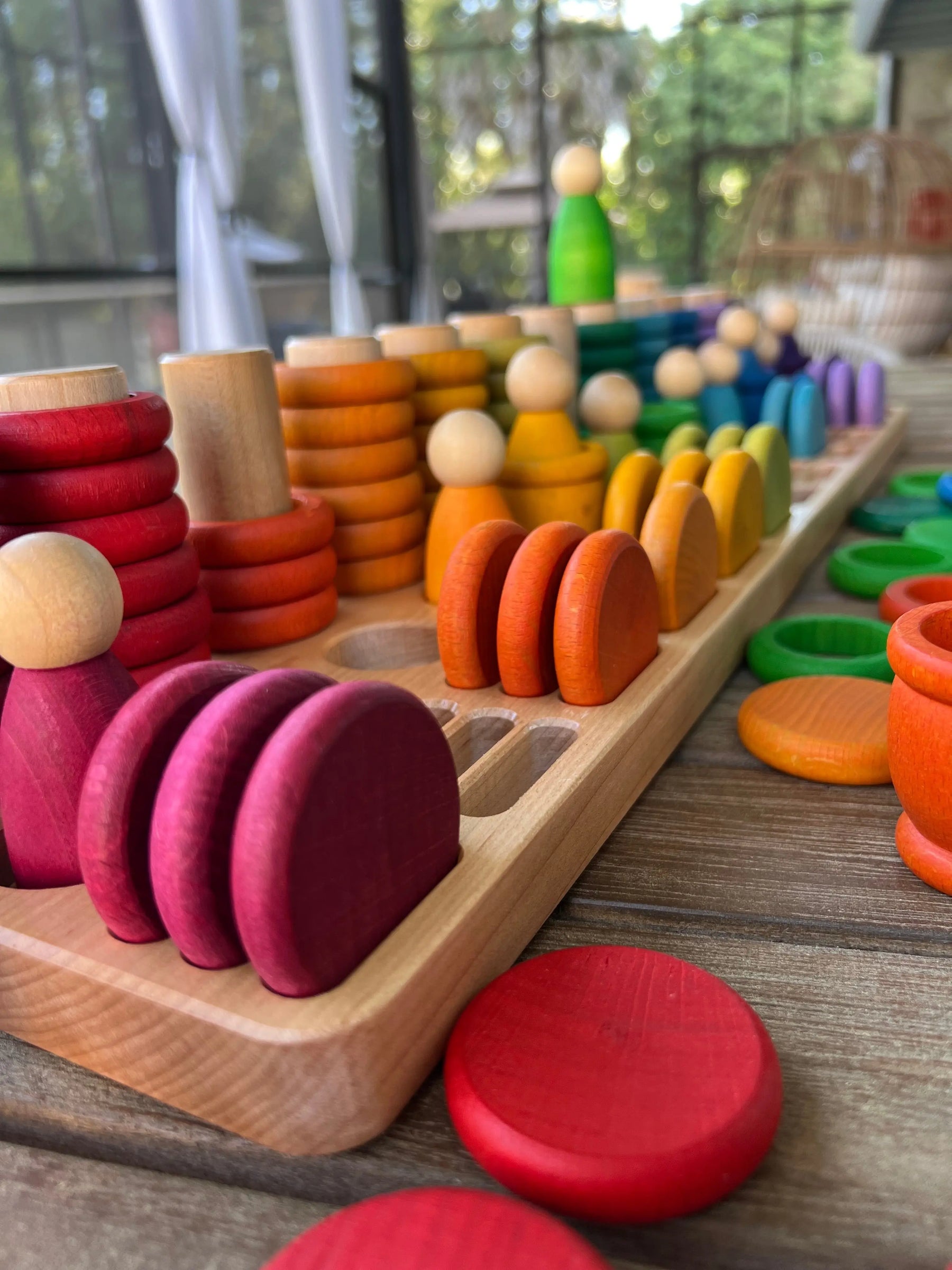 Wooden sorting tray with colorful wooden toy pieces on a wooden surface.