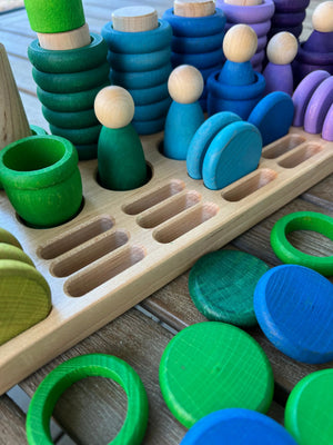 Wooden sorting tray with colored rings and pegs in green, blue, and purple.