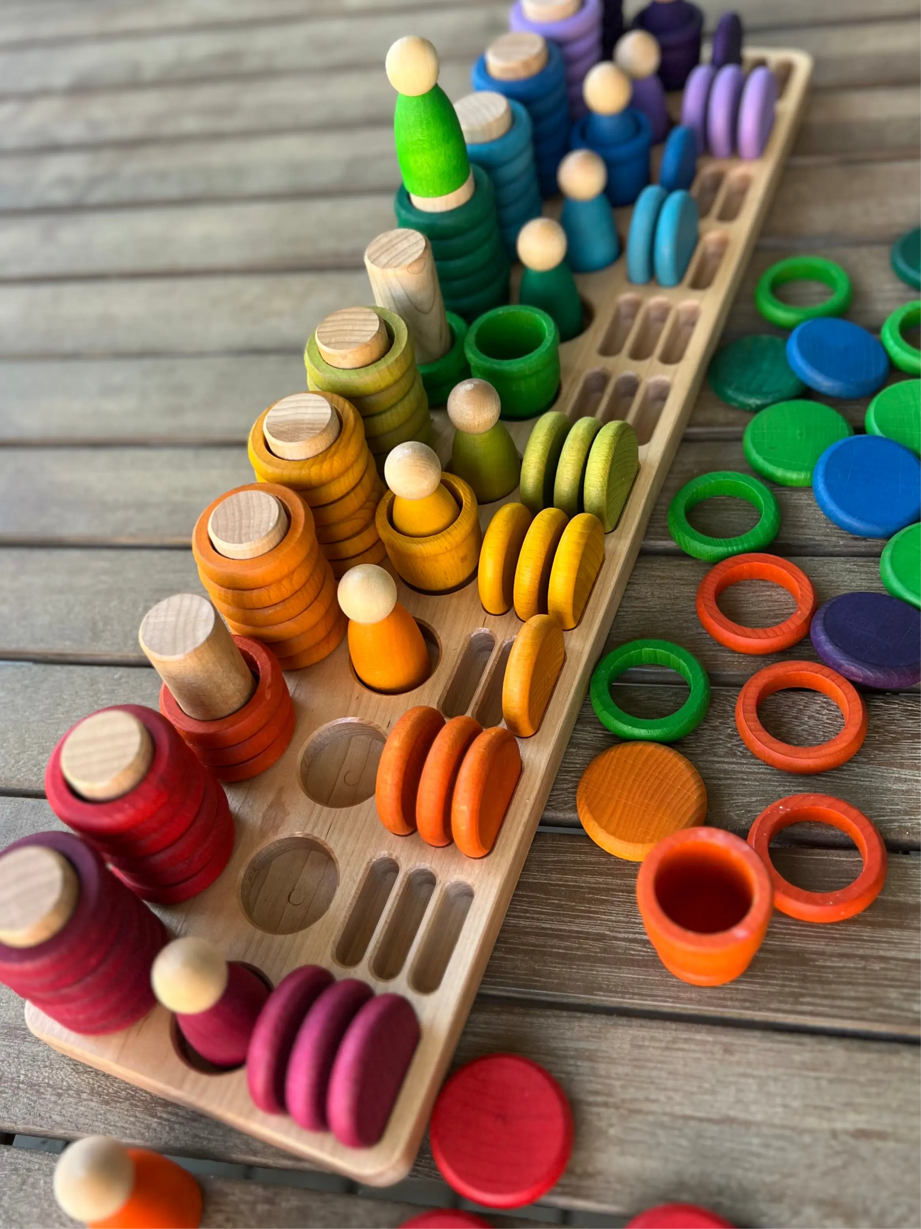 Wooden sorting tray with colorful stacking and peg pieces on a wooden surface.