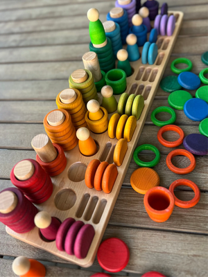 Wooden sorting tray with colorful stacking and peg pieces on a wooden surface.