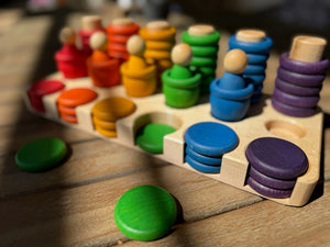 Wooden sorting tray with colorful peg figures and discs in red, orange, yellow, green, blue, and purple.