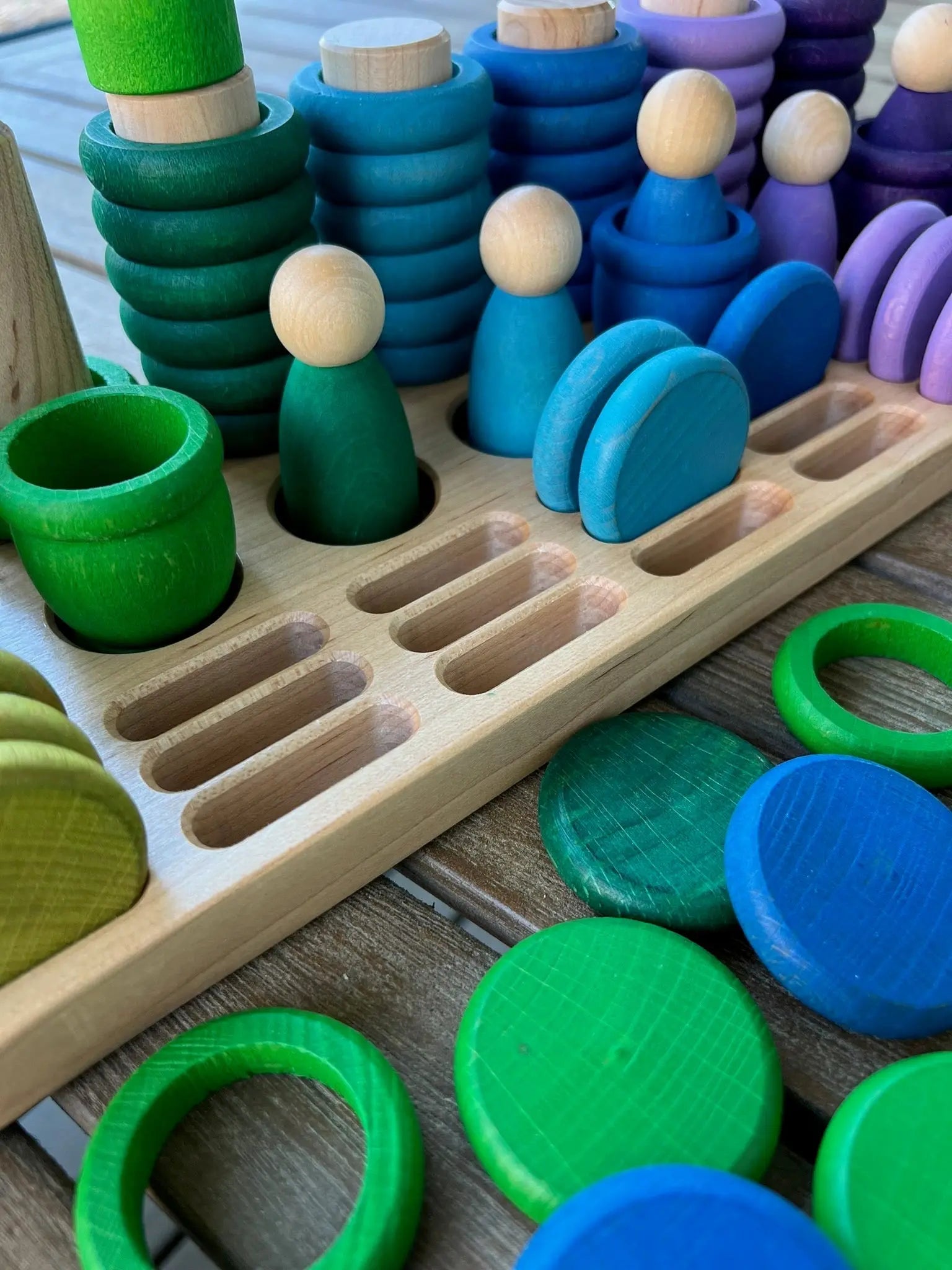 Wooden sorting tray with colorful stacking toys and peg dolls.