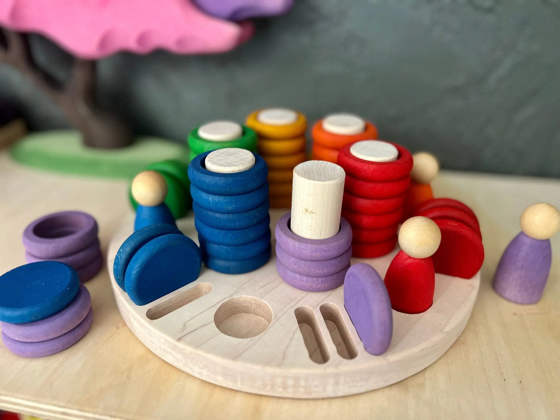 Wooden sorting tray with colorful stacking rings and peg dolls.