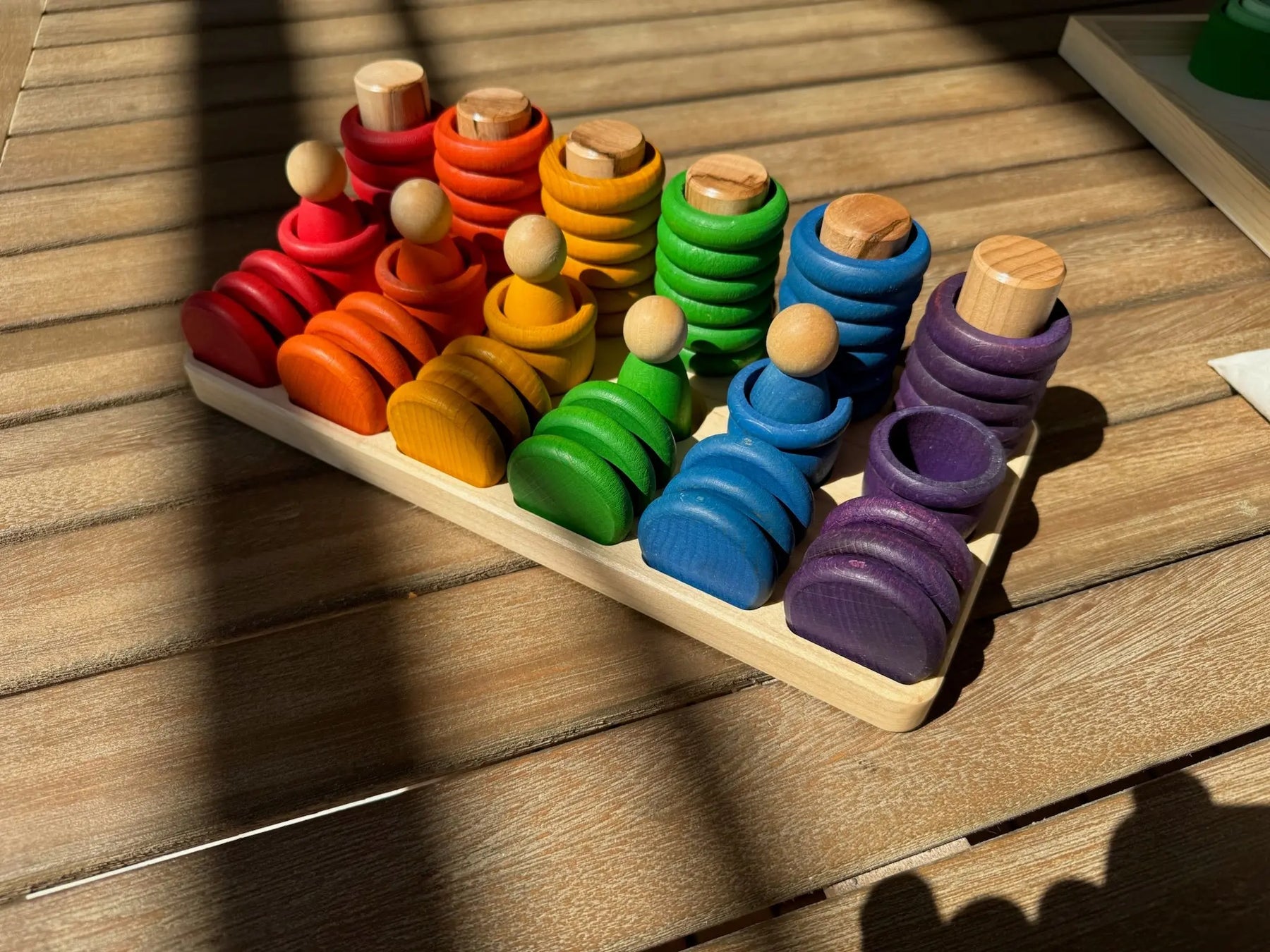 Maple wooden sorting tray with rainbow colored stacking toys on a wooden surface.