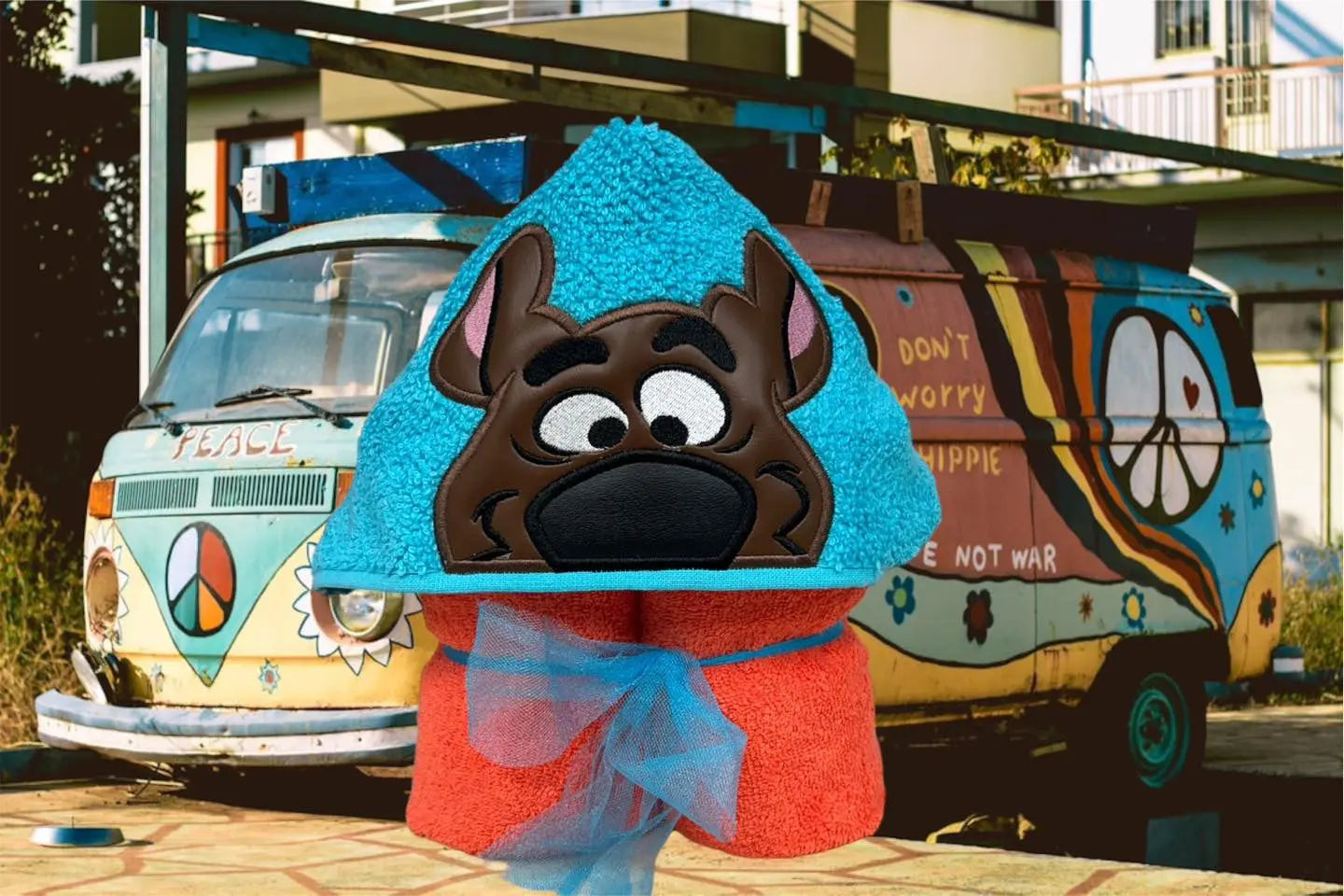 Mystery Dog hooded towel featuring a cartoon dog face on a blue hood with an orange towel and blue ribbon in front of a vintage van.