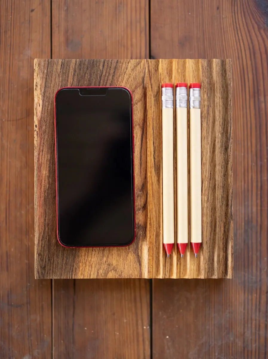 Red phone and three pencils on a textured wood tray sitting on a wooden table.