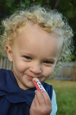 Child with curly blonde hair applying peppermint lip balm with SPF 15