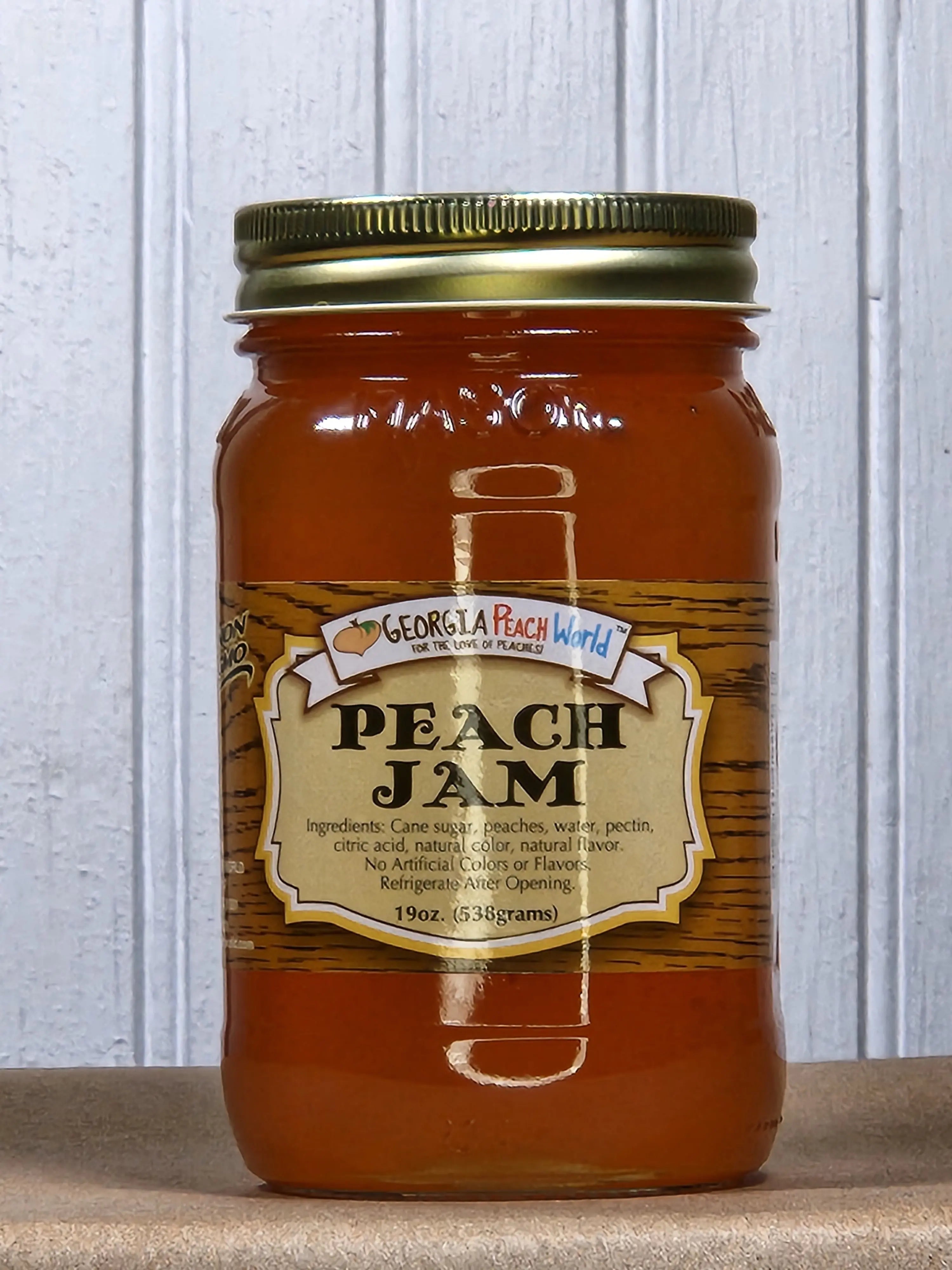 Glass jar of Georgia Peach World peach jam with ingredients and net weight visible on the label.