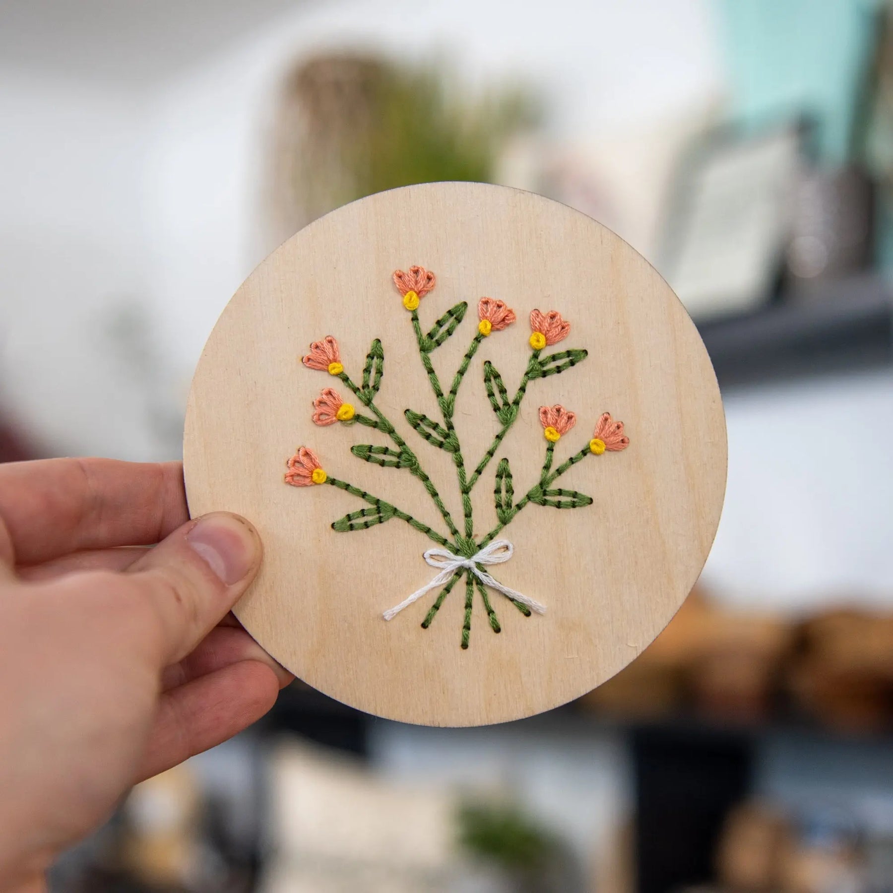 Hand holding wood disk with embroidered flower bouquet.