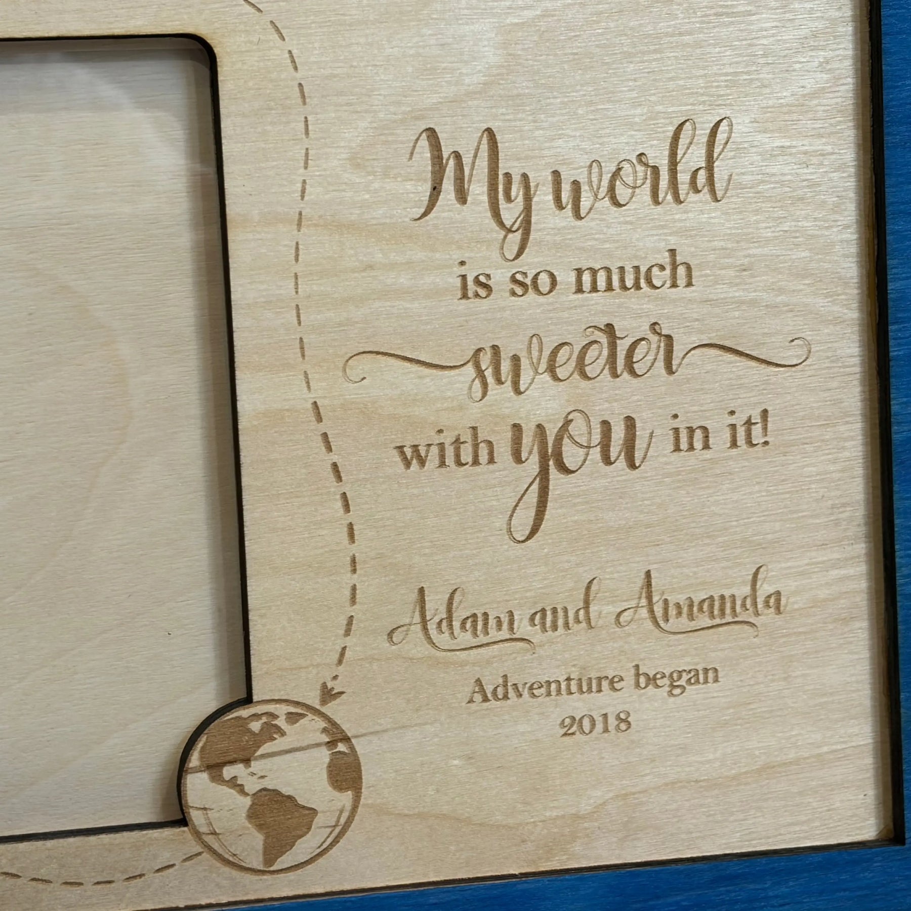 Personalized wooden frame with engraved quote \"My world is so much sweeter with you in it!\", names Adam and Amanda, and globe detail.