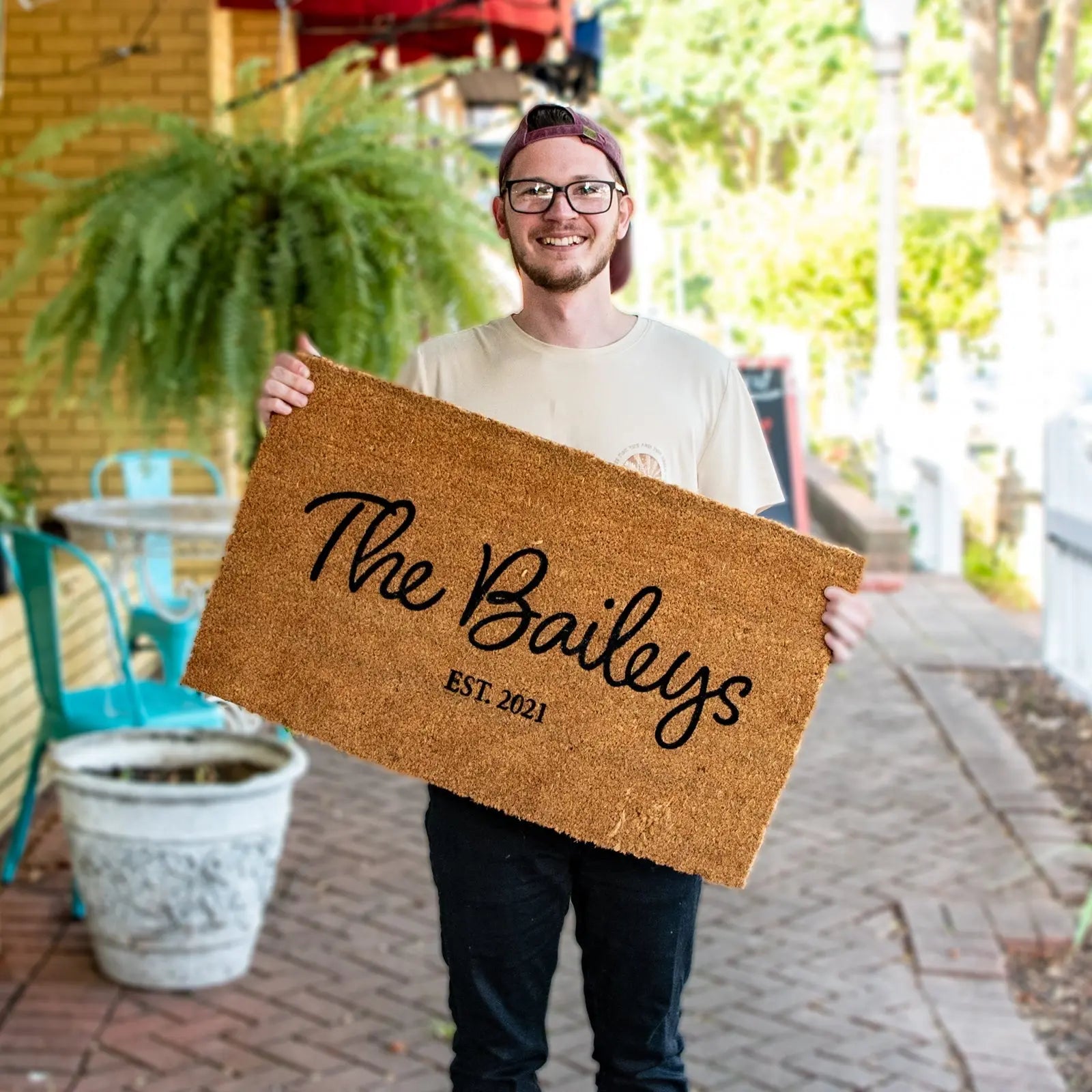 Man holding a personalized doormat with "The Baileys EST. 2021" written on it.