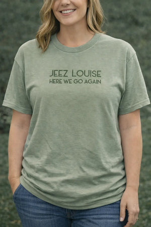 Woman wearing a green t-shirt with the phrase "JEEZ LOUISE HERE WE GO AGAIN" printed in dark green.
