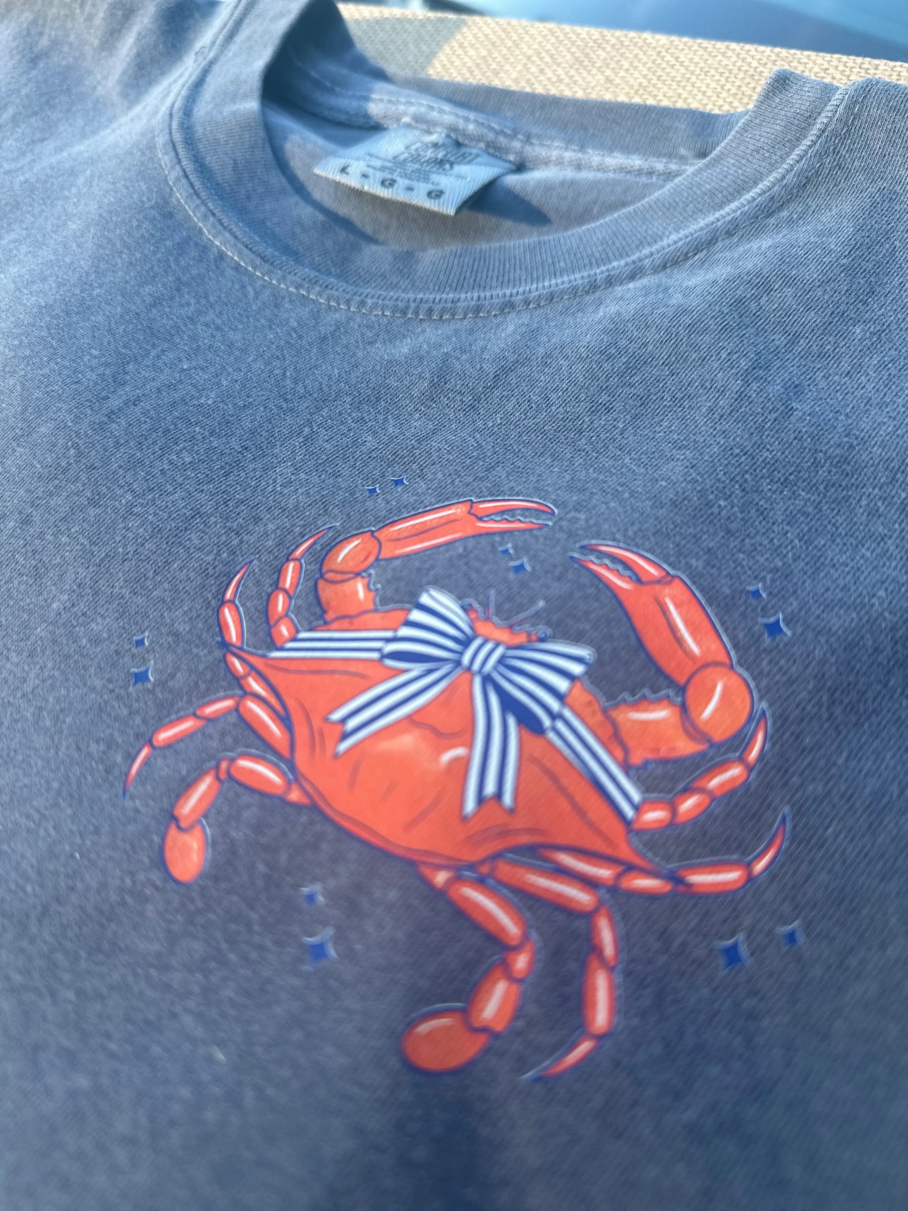 Blue t-shirt with an orange crab graphic wearing a striped bow.