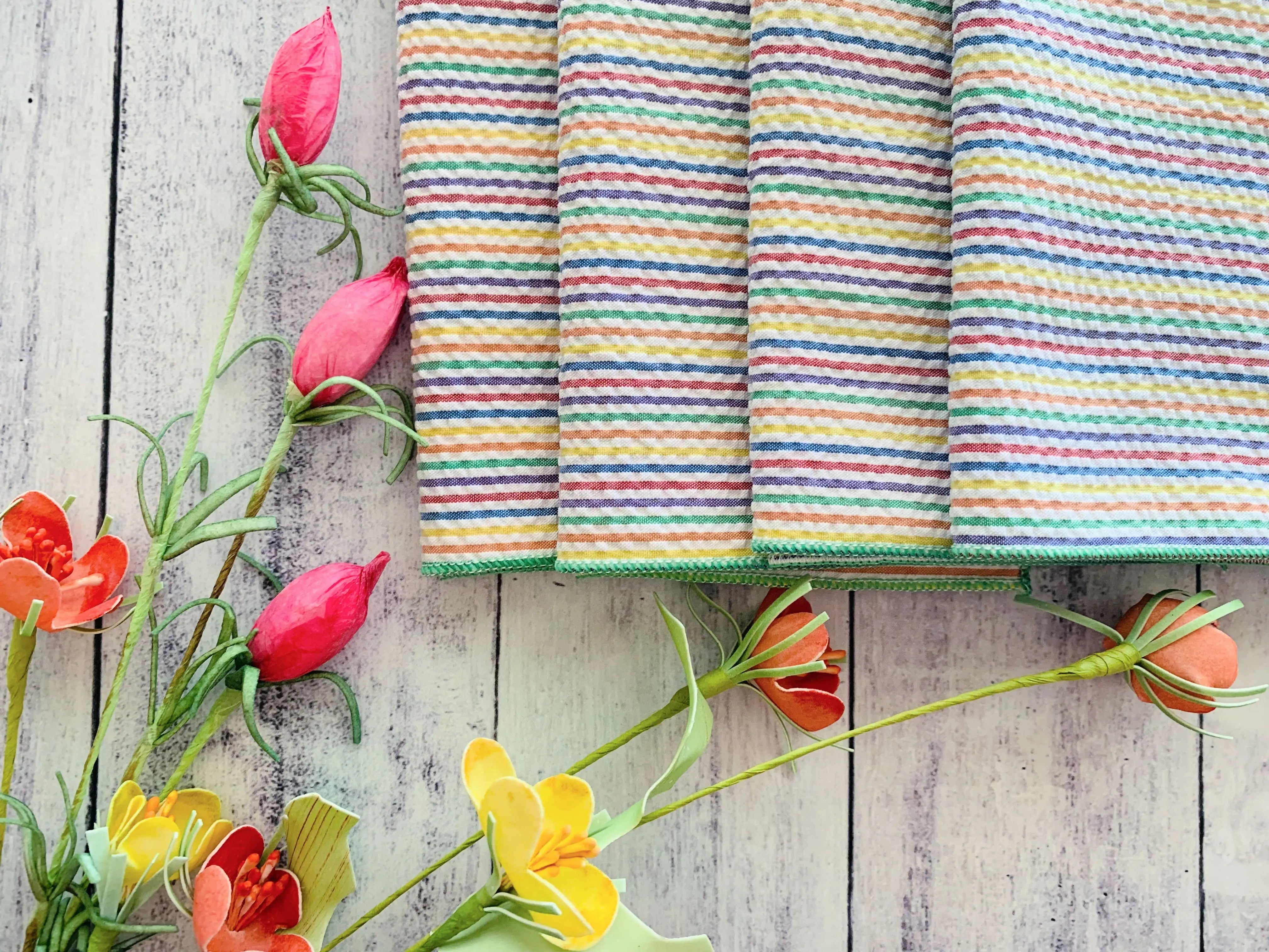 Rainbow striped seersucker cloth napkins with pink and orange paper flowers on a wooden background.