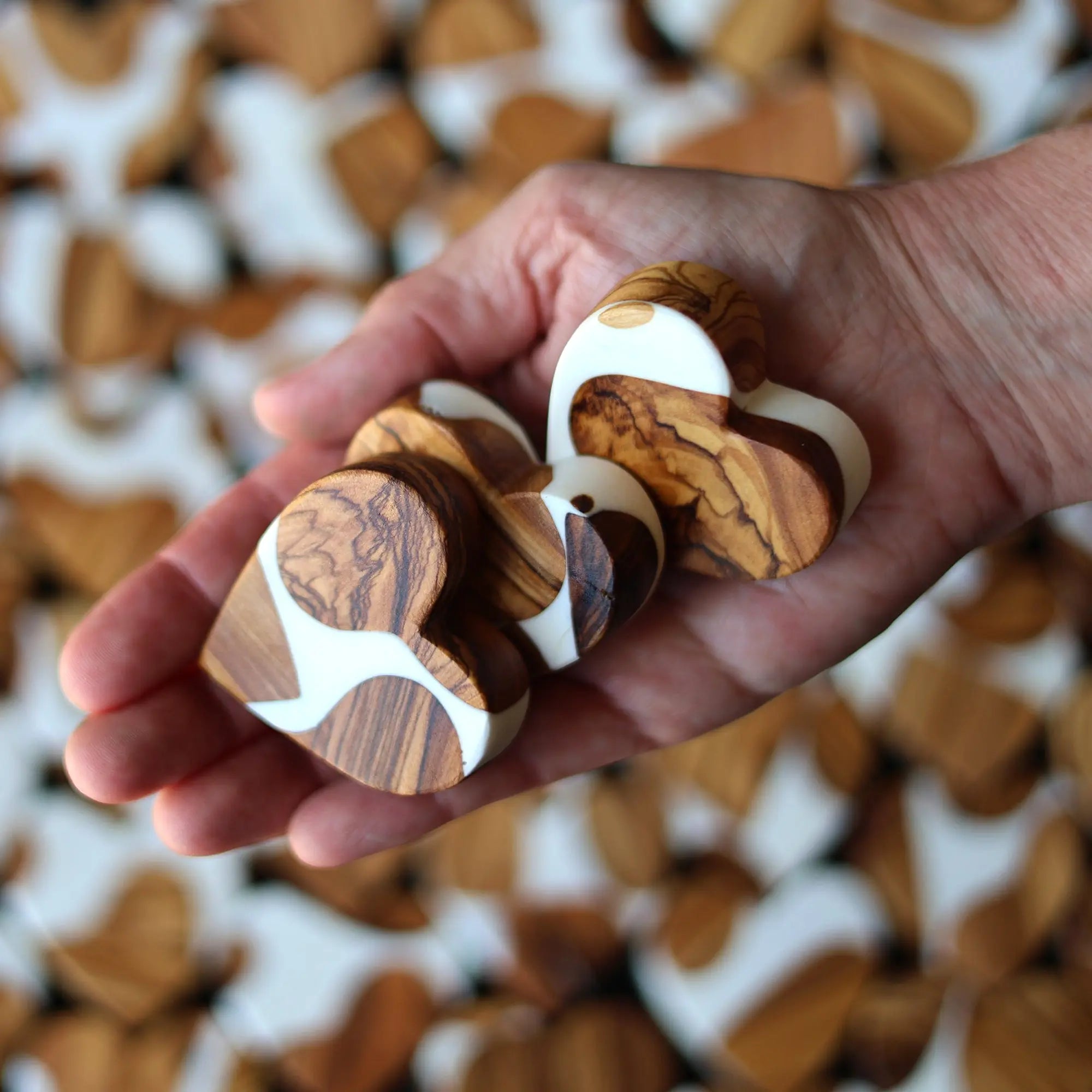 Hand holding wooden and white resin heart shapes