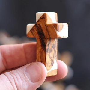 Olive wood and white resin inlay pocket cross held in a hand.