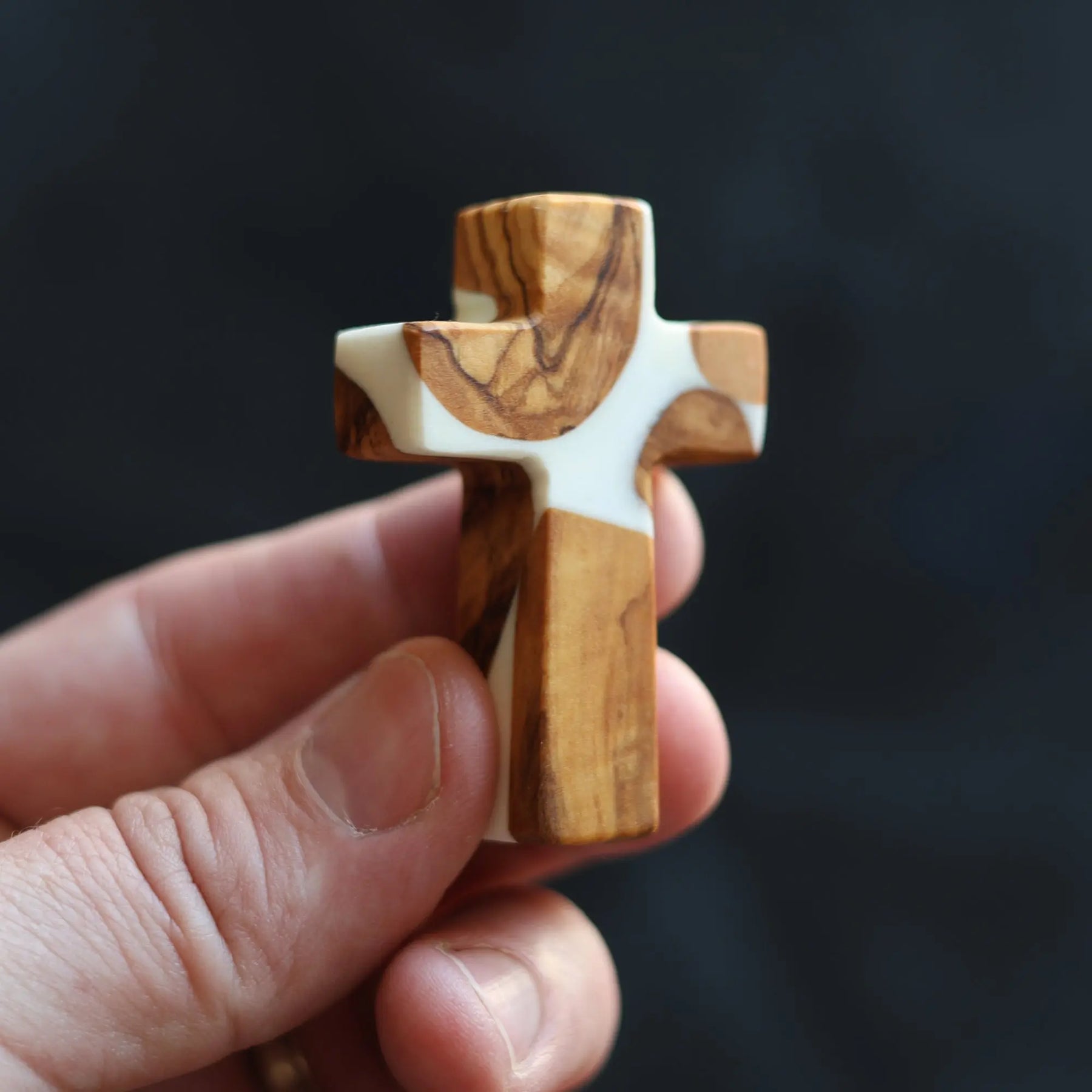 Hand holding a small cross made of olive wood and white resin